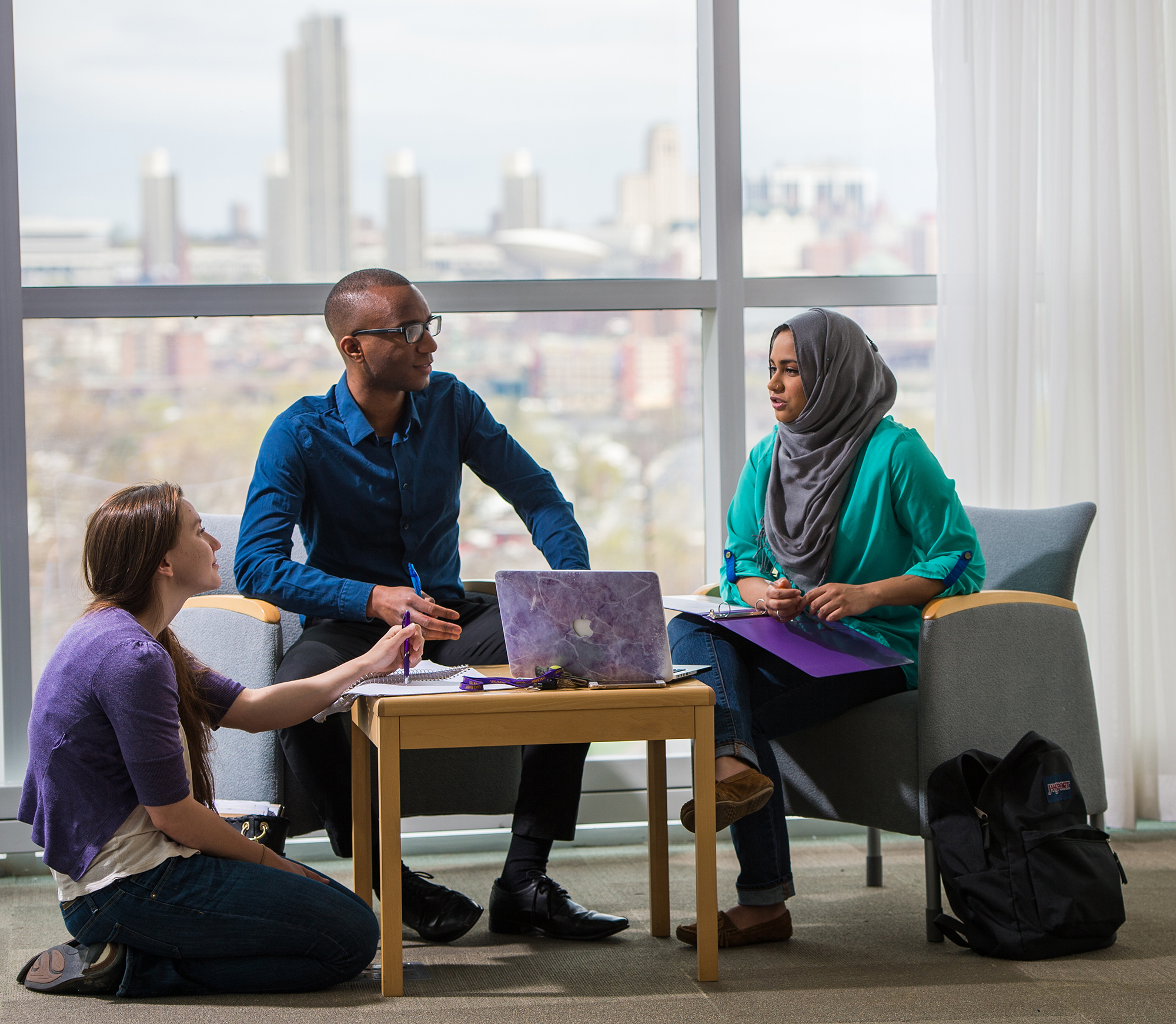 two women and a man sit around a laptop indoors.