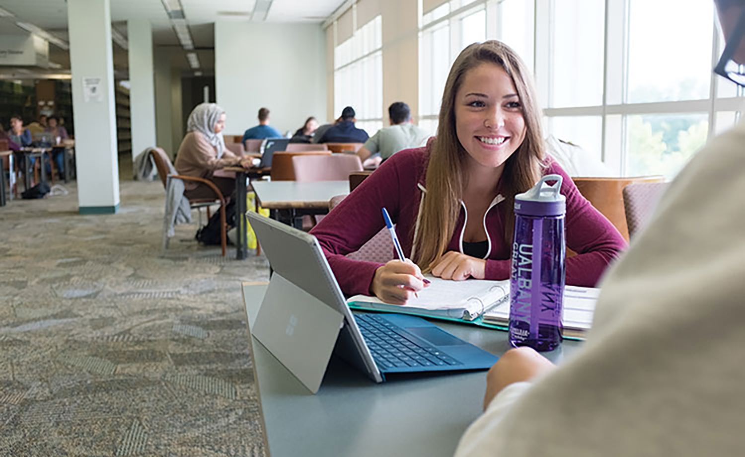 girl at library uses smart device seated at desk with pen in hand